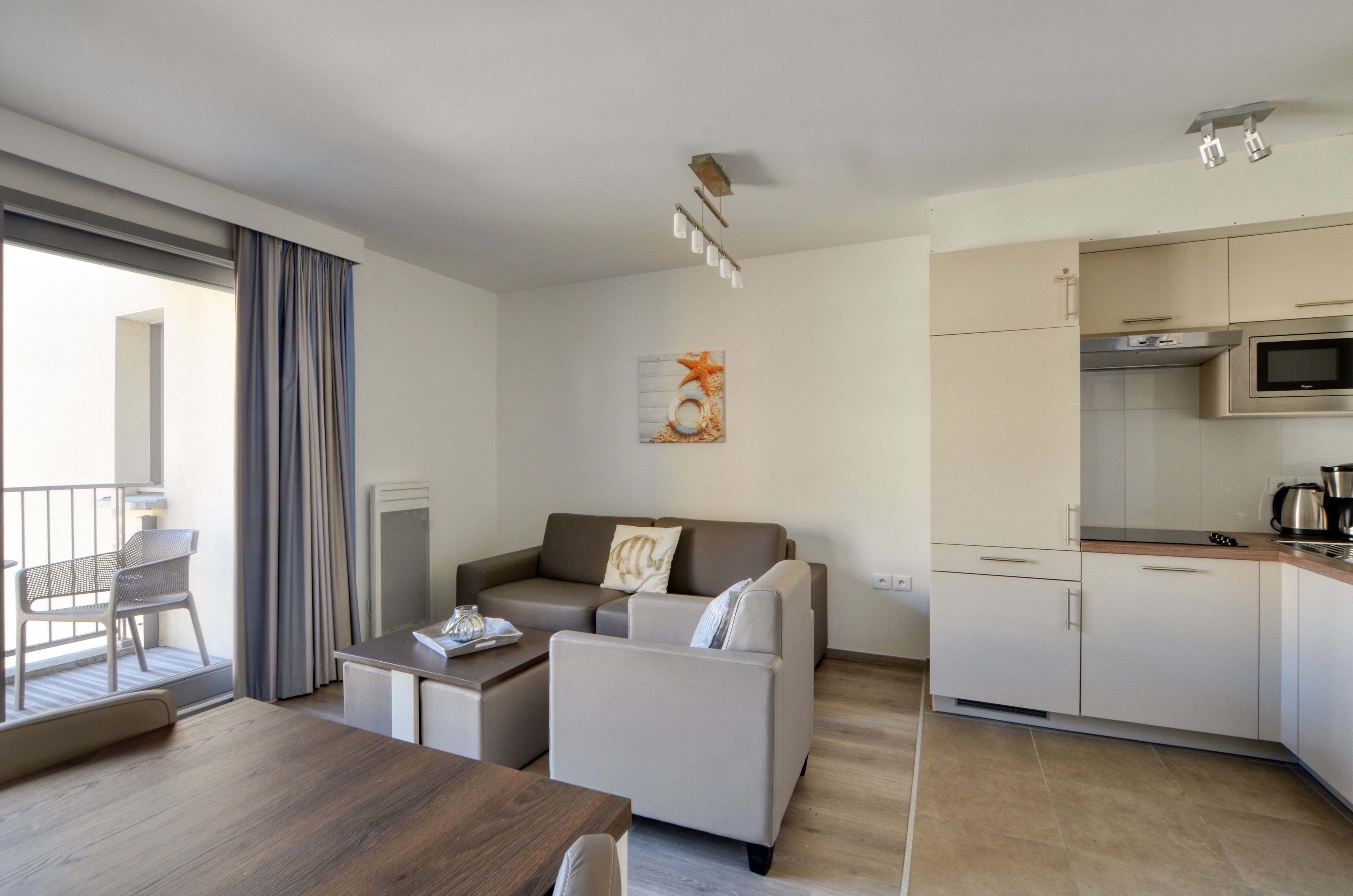 A modern living area with a sofa, coffee table, and dining table. A kitchen with a microwave and stove is visible.