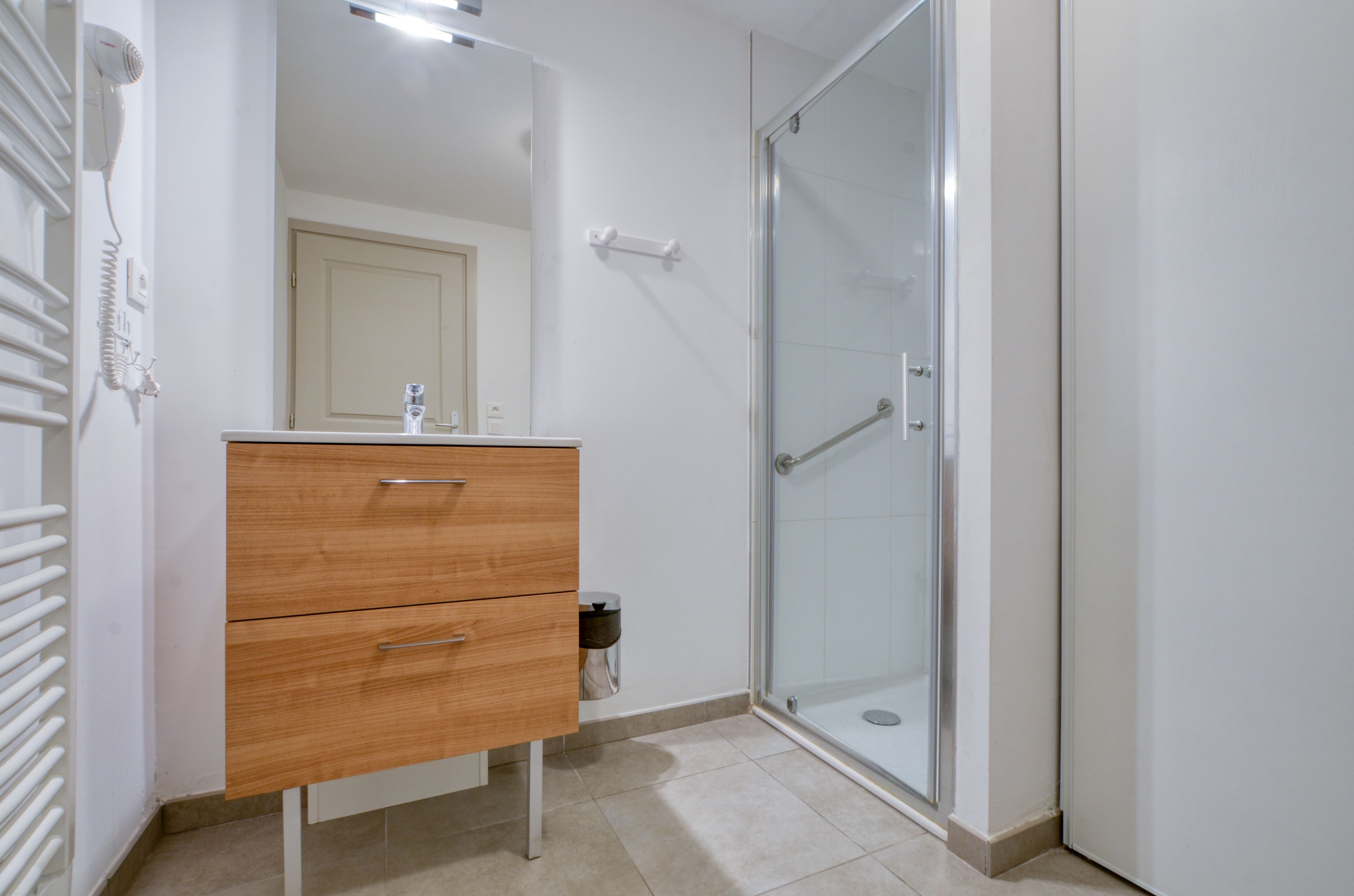 A bathroom with a wooden vanity, a glass shower enclosure, and a white door.