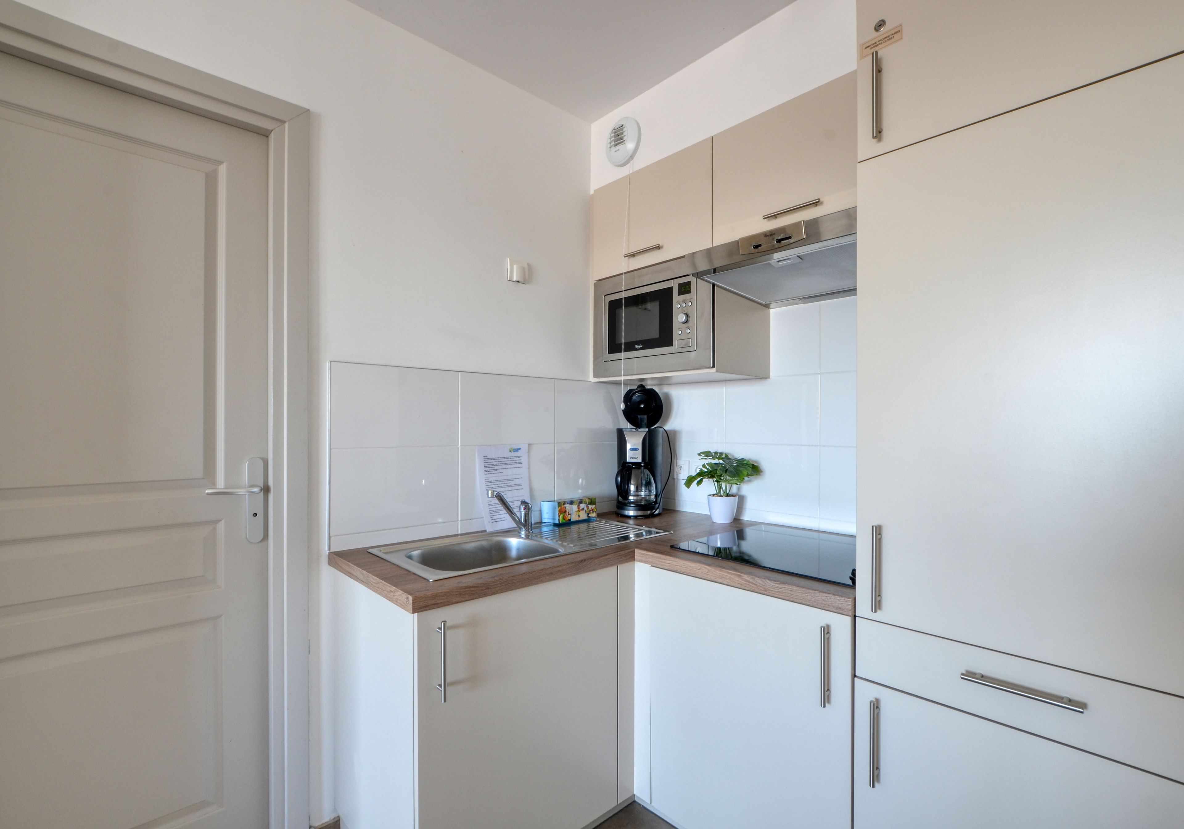 A compact kitchen with a microwave, coffee maker, sink, and cabinets.