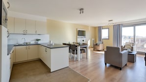 A modern apartment with a kitchen, dining area, and living room. It features a large window, a flat-screen TV, and a balcony with outdoor furniture. - Evancy Etoile des Dunes (Bray-Dunes)