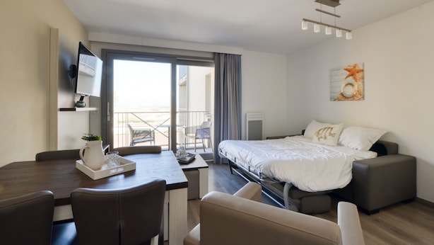 A modern hotel room with a bed, a desk, and a chair. There is a TV mounted on the wall and a window with curtains. - Evancy Etoile des Dunes (Bray-Dunes)