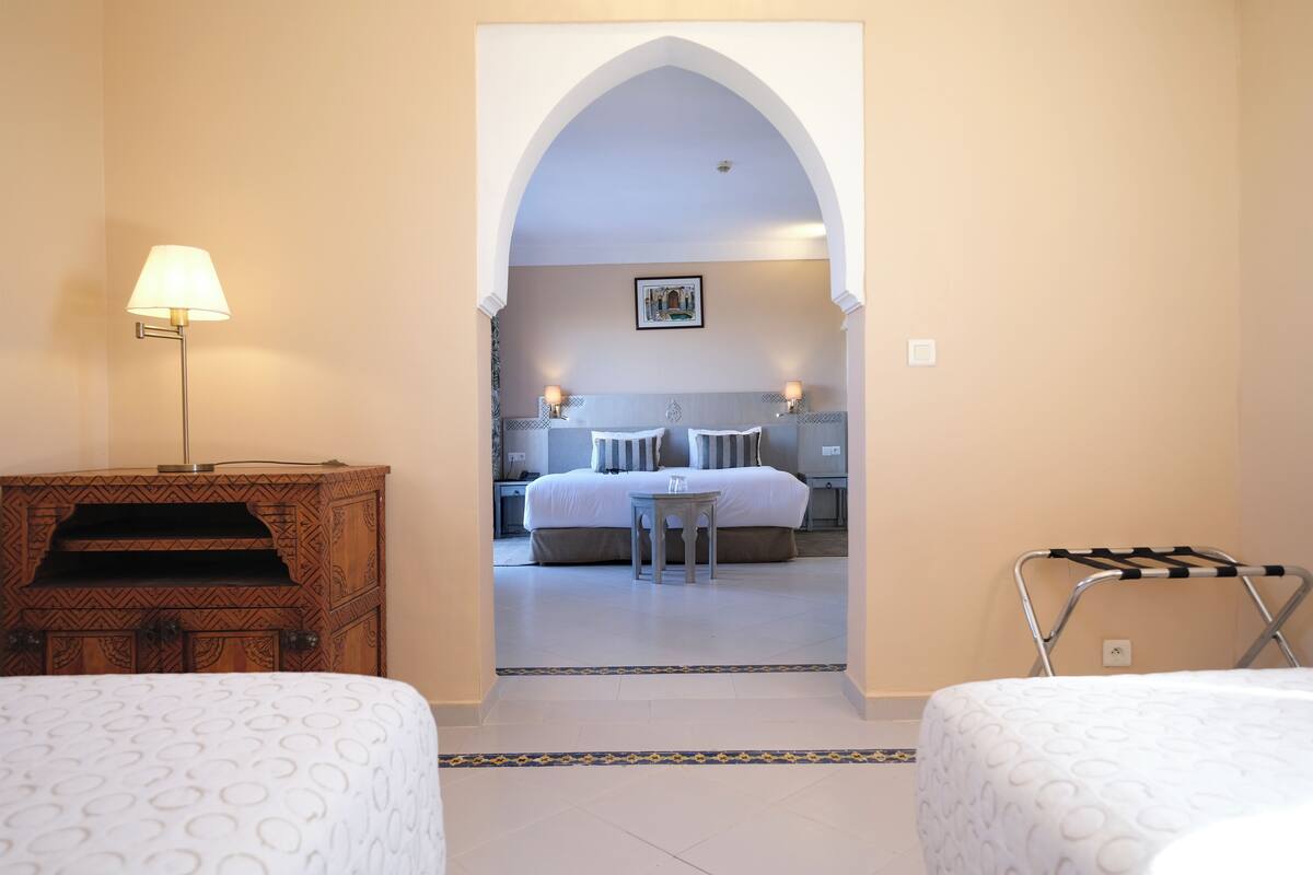 Una habitación de hotel con una cama, una mesita pequeña, una lámpara y un armario de madera.