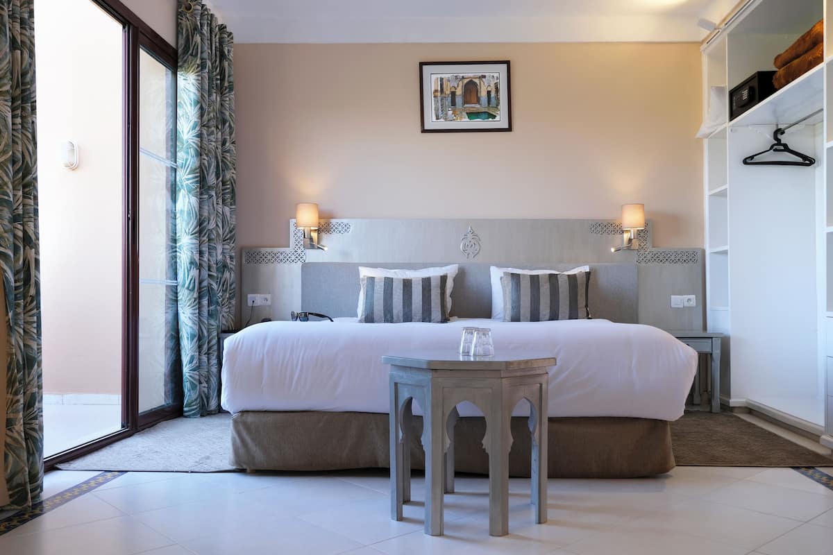 Habitación de hotel ordenada con una cama grande, lámparas de noche, una mesita y un cuadro en la pared.