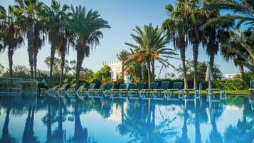 Relax by the serene pool surrounded by lush palm trees and lounge chairs.