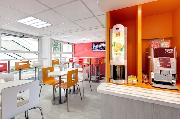 A modern cafe with white and orange chairs, a Nescafe coffee machine, and a large window with a view of the outside.