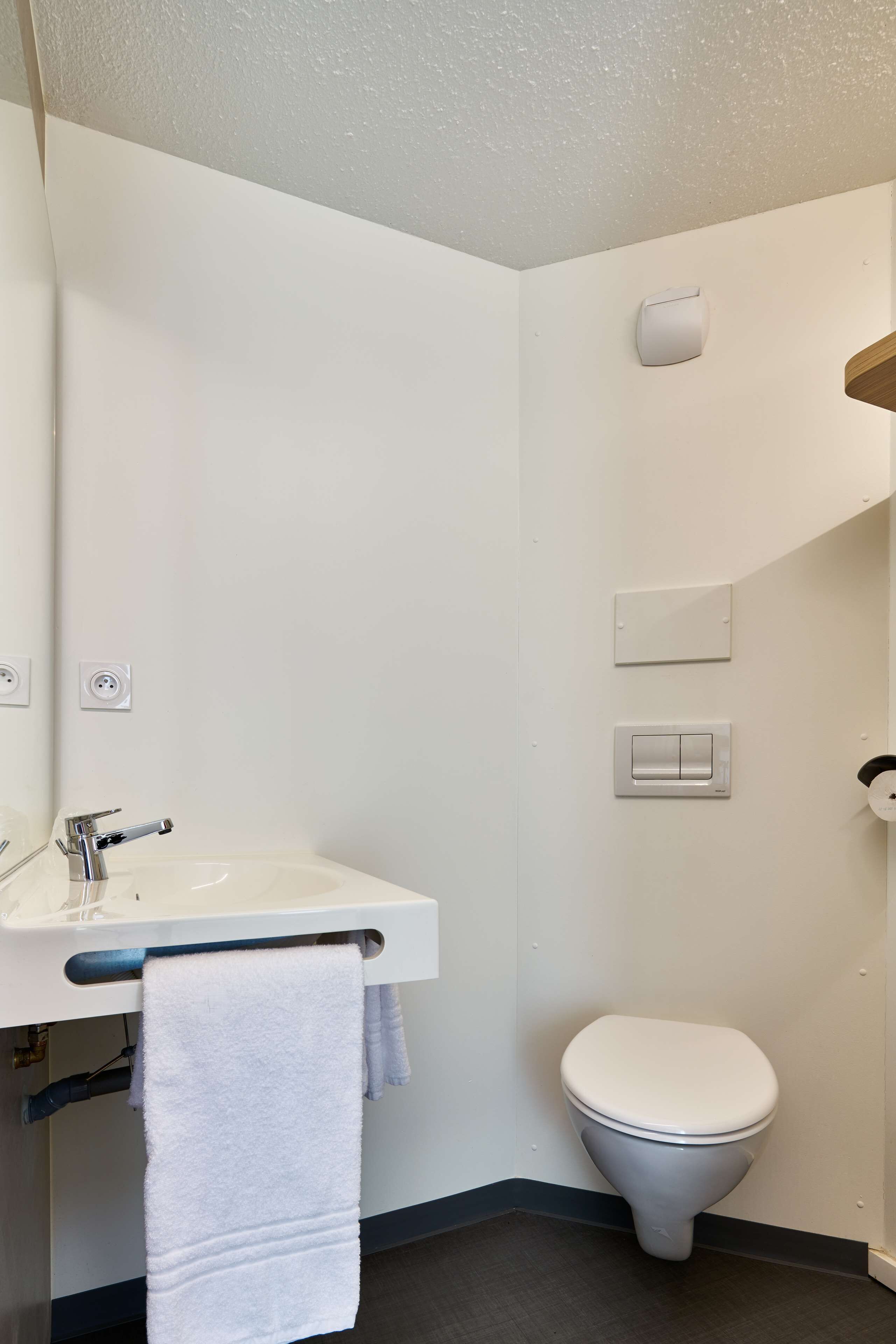 Un baño pequeño y moderno con un lavamanos blanco, una toalla colgada en la pared, un inodoro y un interruptor de luz.