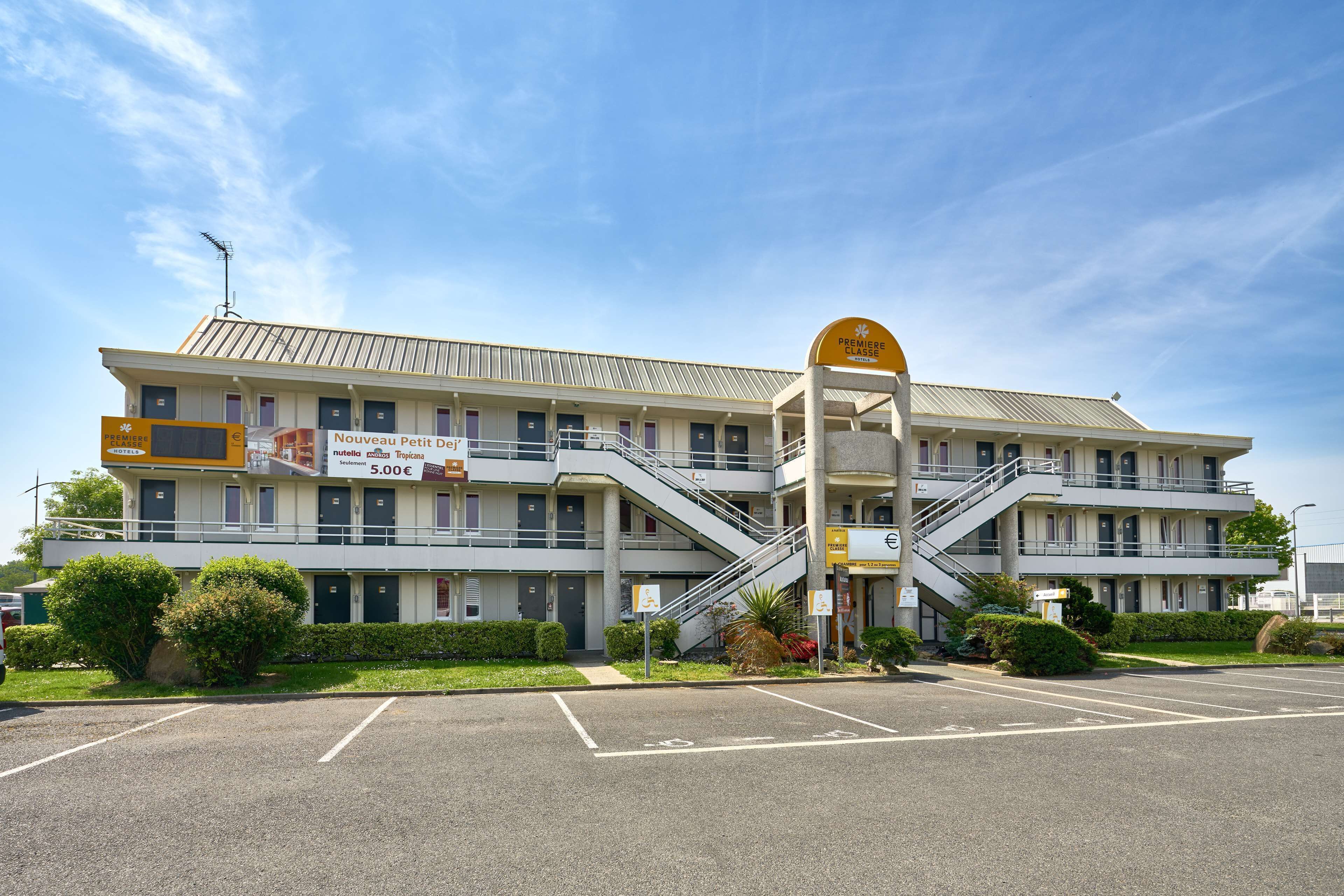 A multi-story hotel with a central staircase, a sign for "Nouveau Petit Désert," and a parking lot.