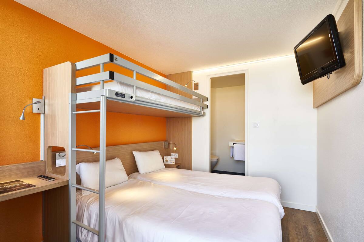 Un lit superposé avec un bureau et un téléviseur fixé au mur.