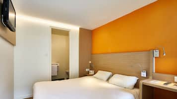 A hotel room with a bed, bedside table, lamp, and a TV mounted on the wall.