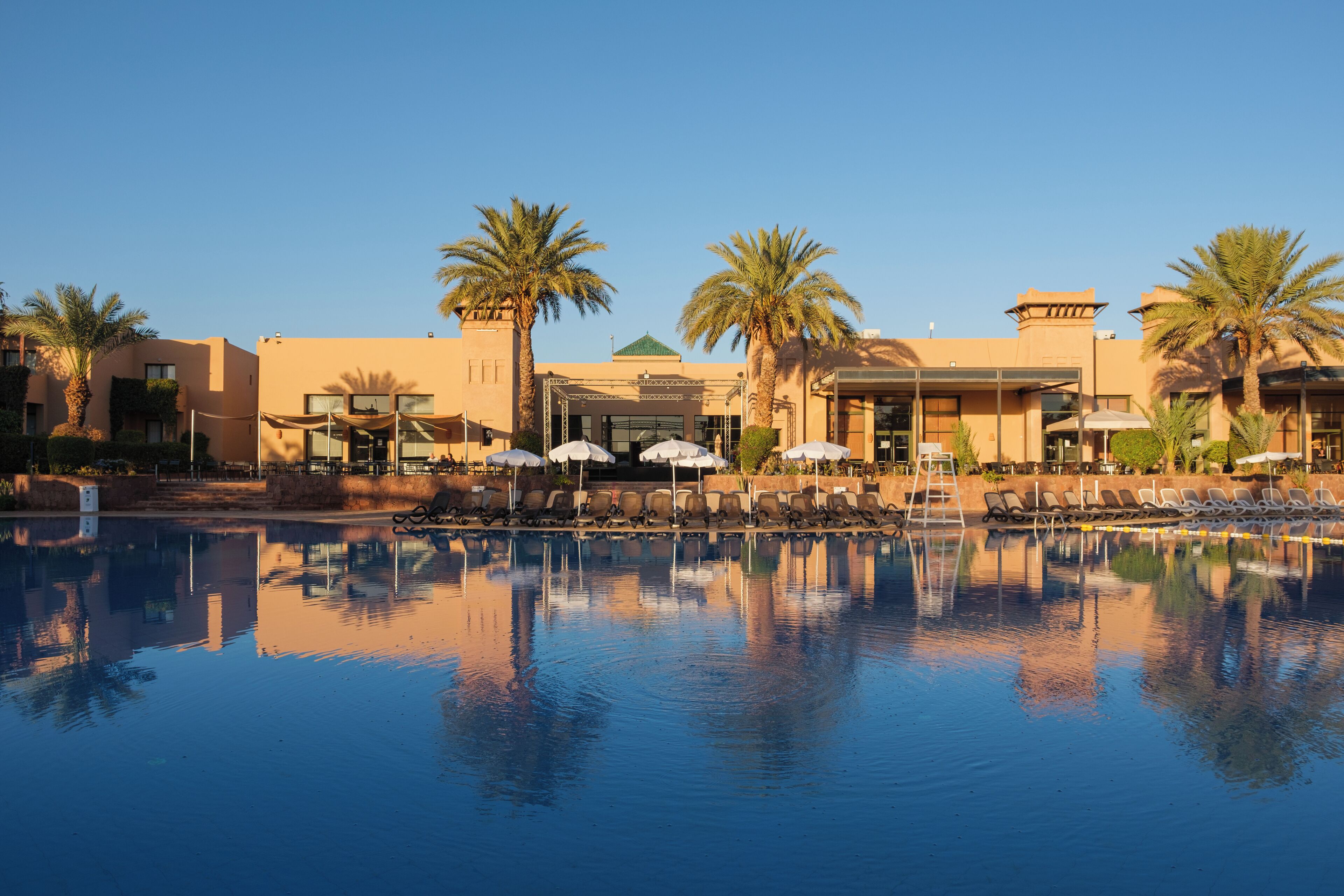 A hotel with a swimming pool, palm trees, and sun loungers.