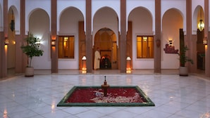 Un hall d’hôtel doté d’une fontaine centrale, d’arcades et de plantes en pot.