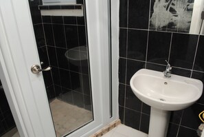 A bathroom with black tiled walls, a white sink, and a glass shower enclosure. - Mango Beach Studio (Negril)