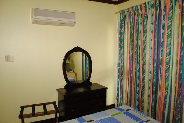 A bedroom with a bed, a dresser with a mirror, a wall-mounted air conditioner, and a curtain with a leaf pattern. - Crawfish Beach Suite (Negril)