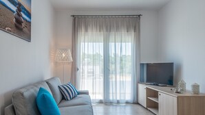 Una sala de estar moderna con un sofá, televisor y vistas a través de un ventanal grande.