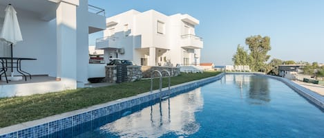 A modern hotel with a swimming pool, outdoor seating, and a clear view of the sea.