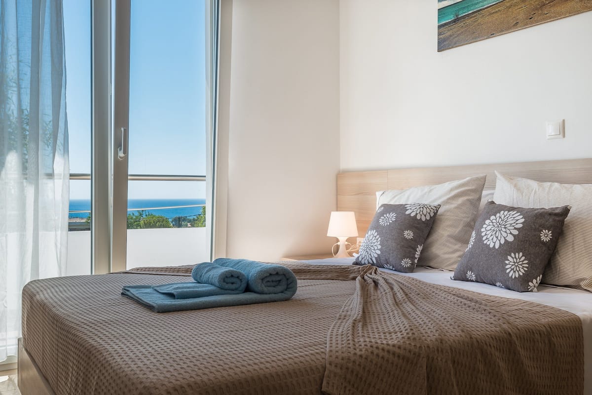 Un cuarto de hotel con una cama, vista al mar y un cuadro en la pared.