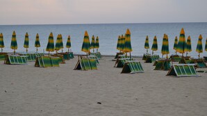 A beach with rows of green and yellow beach umbrellas and lounge chairs.