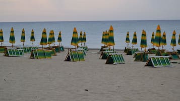 Een privéstrand, wit zand, ligstoelen aan het strand, parasols