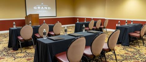 A conference room with tables, chairs, and a projector screen displaying "Mount Vernon Grand".