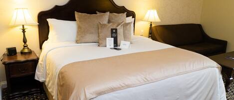 A neatly made bed with a dark headboard, two bedside tables with lamps, a brown leather chair, and a patterned floor.