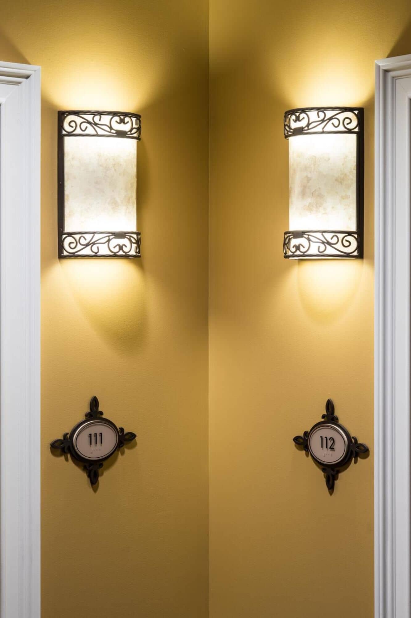 Two doors with numbers 111 and 112, each with a wall-mounted light fixture and a decorative number plate.