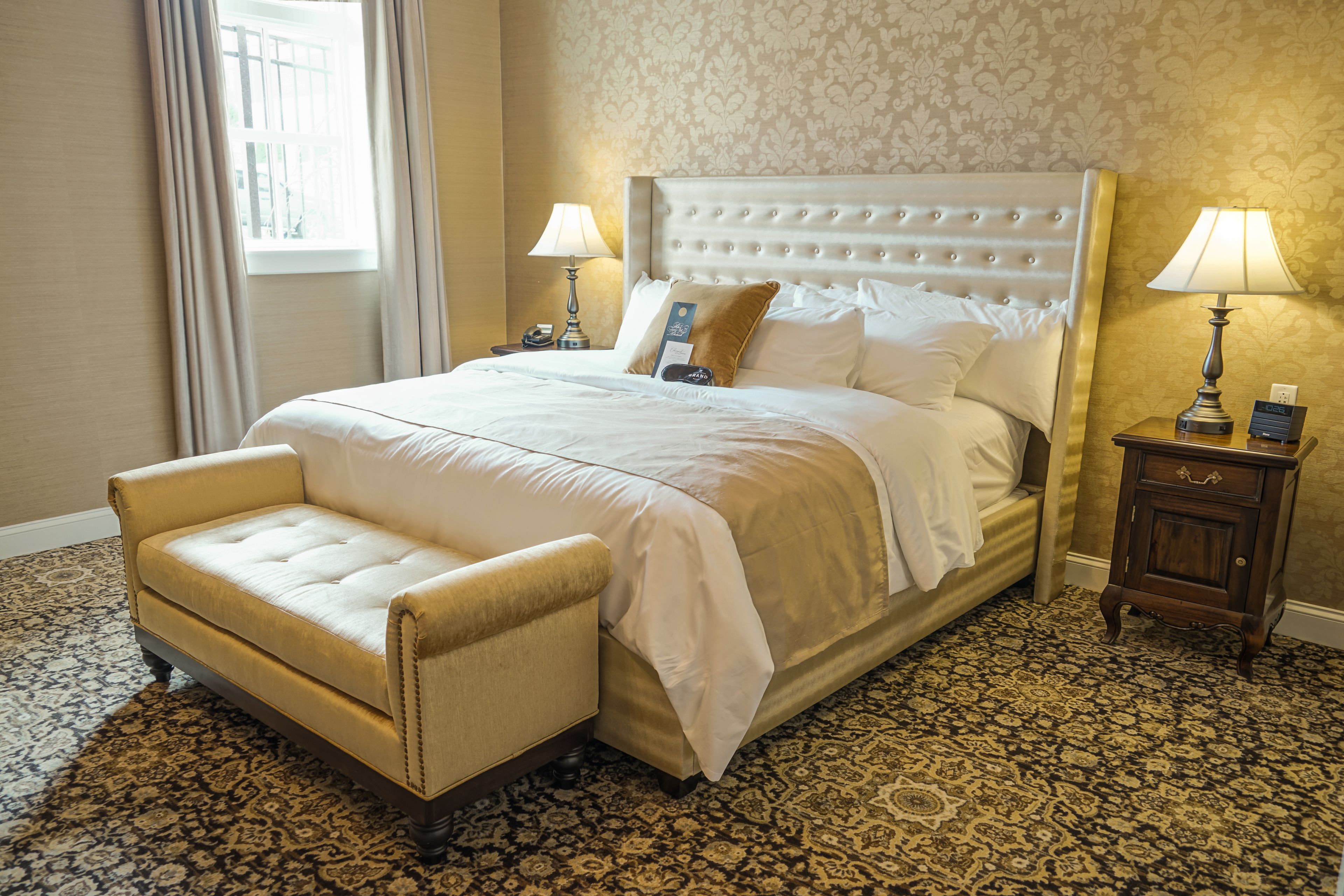 A neatly made bed with a headboard, a bedside table with a lamp, and a chair.