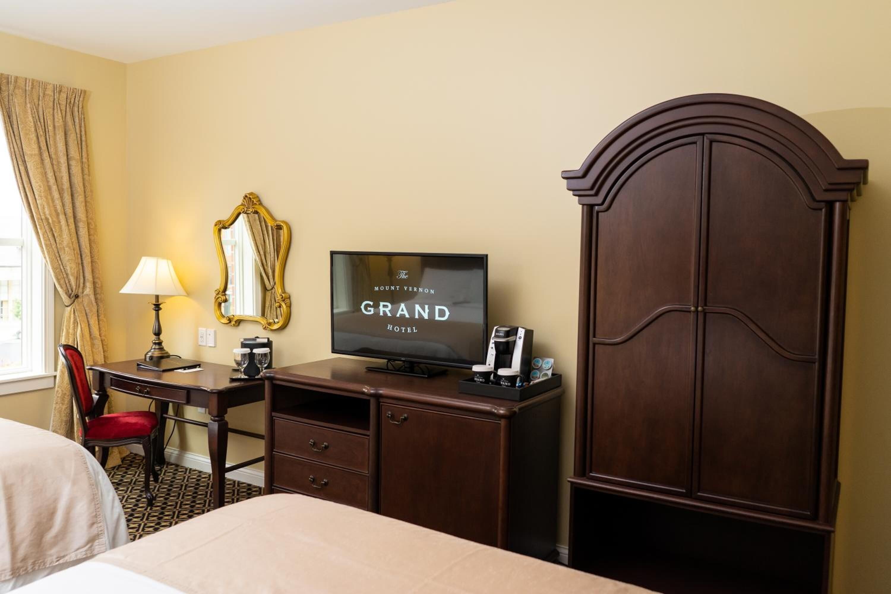 A hotel room with a bed, a desk with a television, a mirror, and a wardrobe.