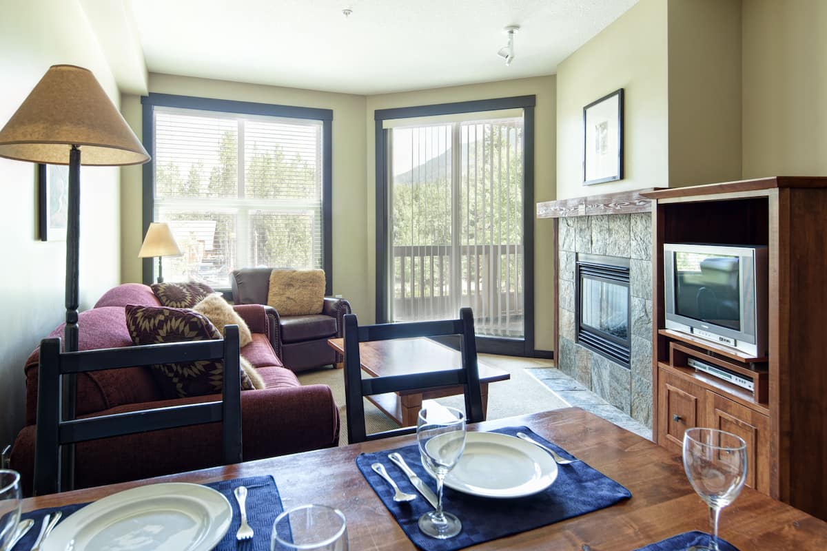 A dining area with a table set for two, a sofa, and a fireplace.