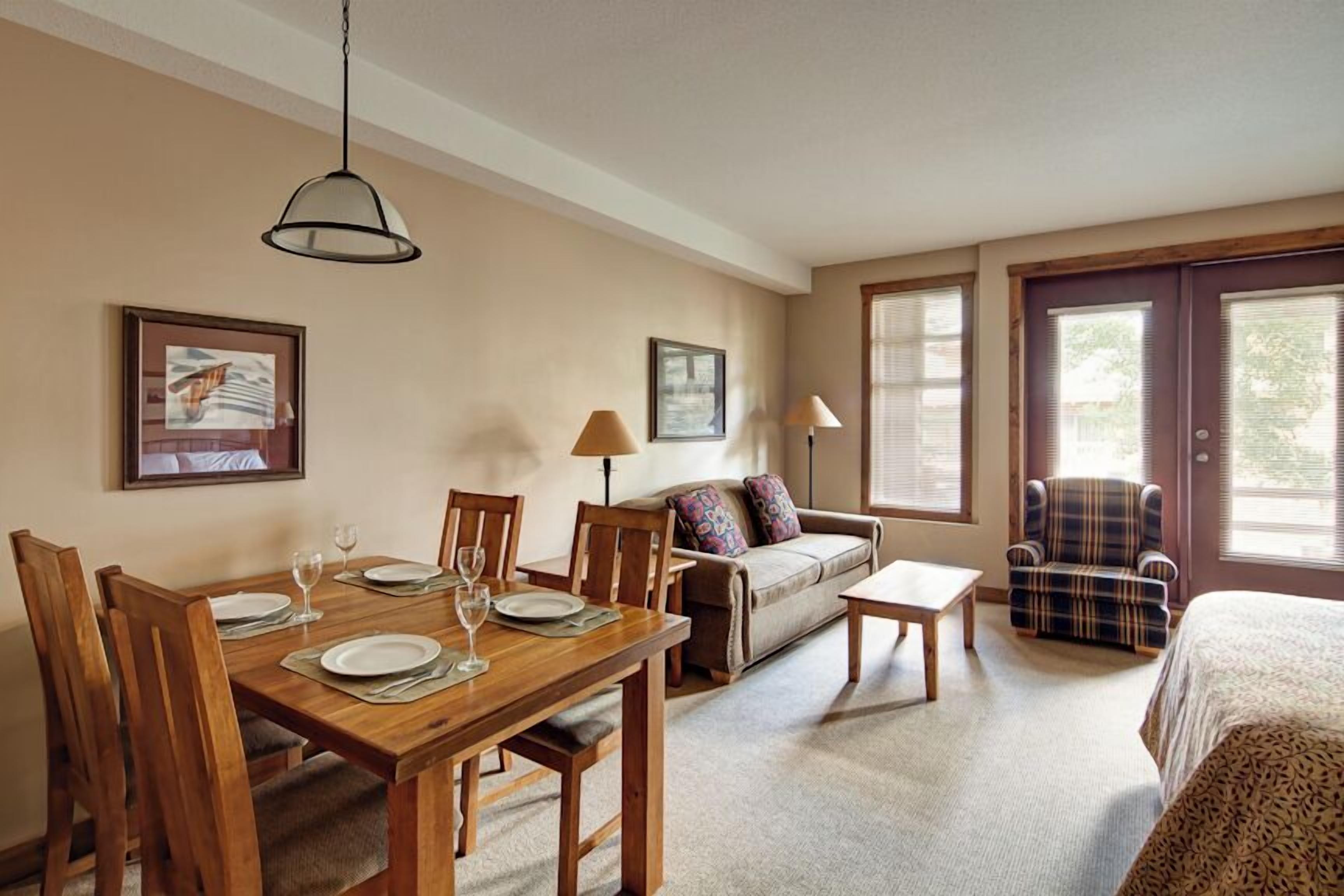 A room with a dining table set for four, a sofa, a chair, and a bed.