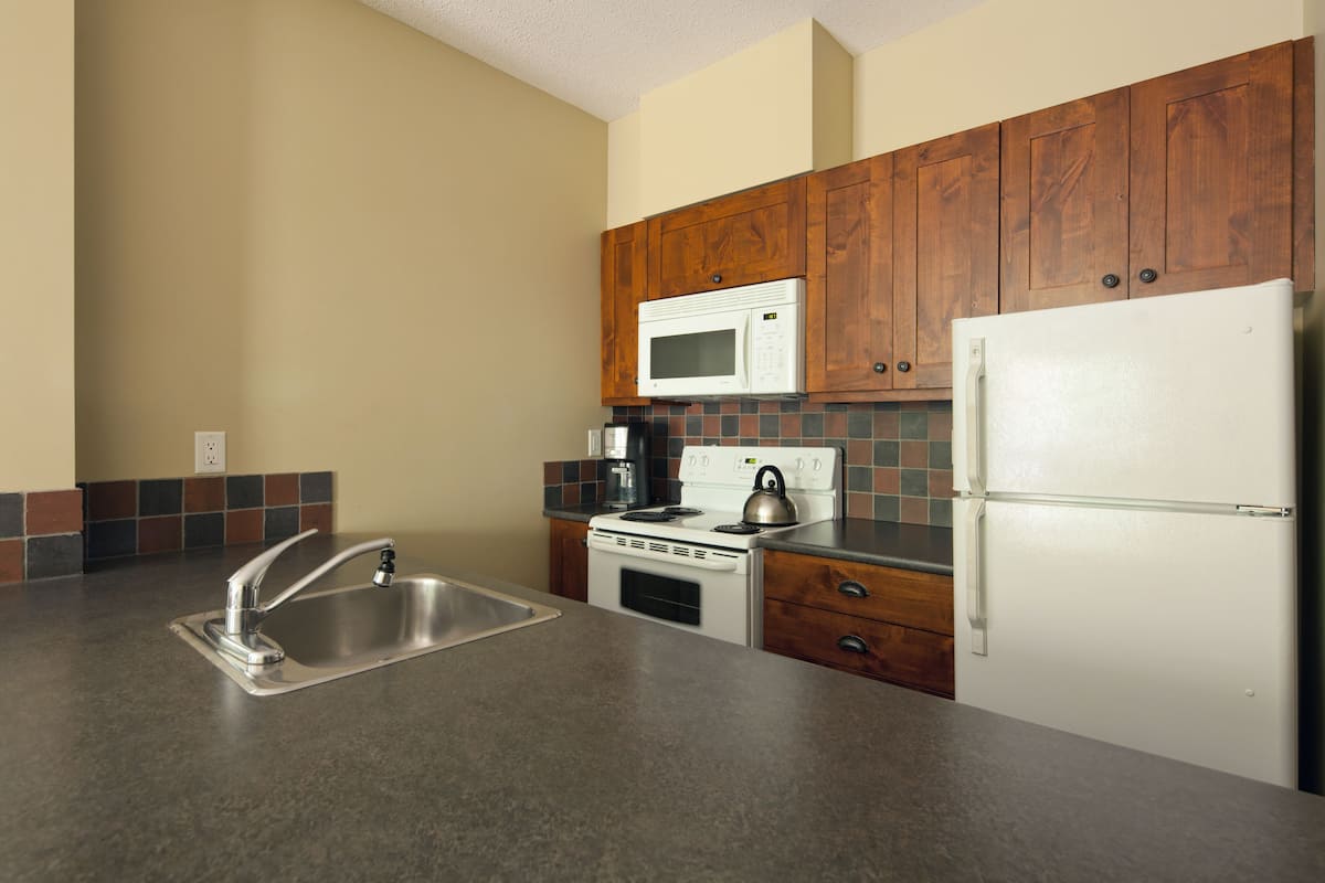 A kitchen with a stainless steel sink, a white stove, a microwave, and a refrigerator.