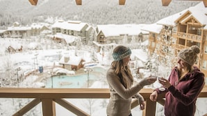 A view from a balcony overlooking a snowy landscape with buildings and a pool. - Panorama Mountain Resort - Premium Condos and Townhomes (Panorama)