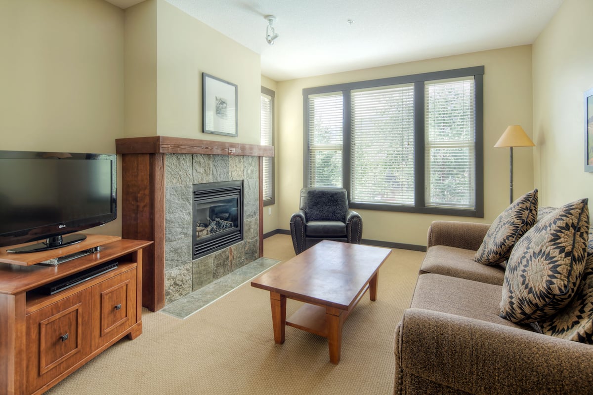 A living room with a fireplace, a television on a wooden stand, a sofa, and a chair.