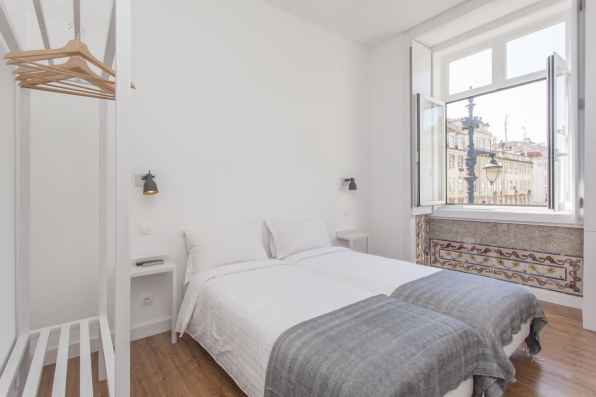 A bedroom with two beds, a window with a view of buildings, and a hanging clothes rack.