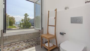 A bathroom with a toilet, a wooden drying rack, a window with a view of the outside, and a tiled floor.
