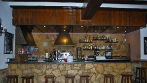 Eine Bar mit einer Steintheke, hölzernen Barhocker, einer Kaffeemaschine und verschiedenen Flaschen.
