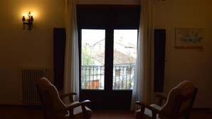 Ein Zimmer mit zwei Stühlen, einem Heizkörper, einem Fenster mit Vorhängen und einer Wandleuchte.