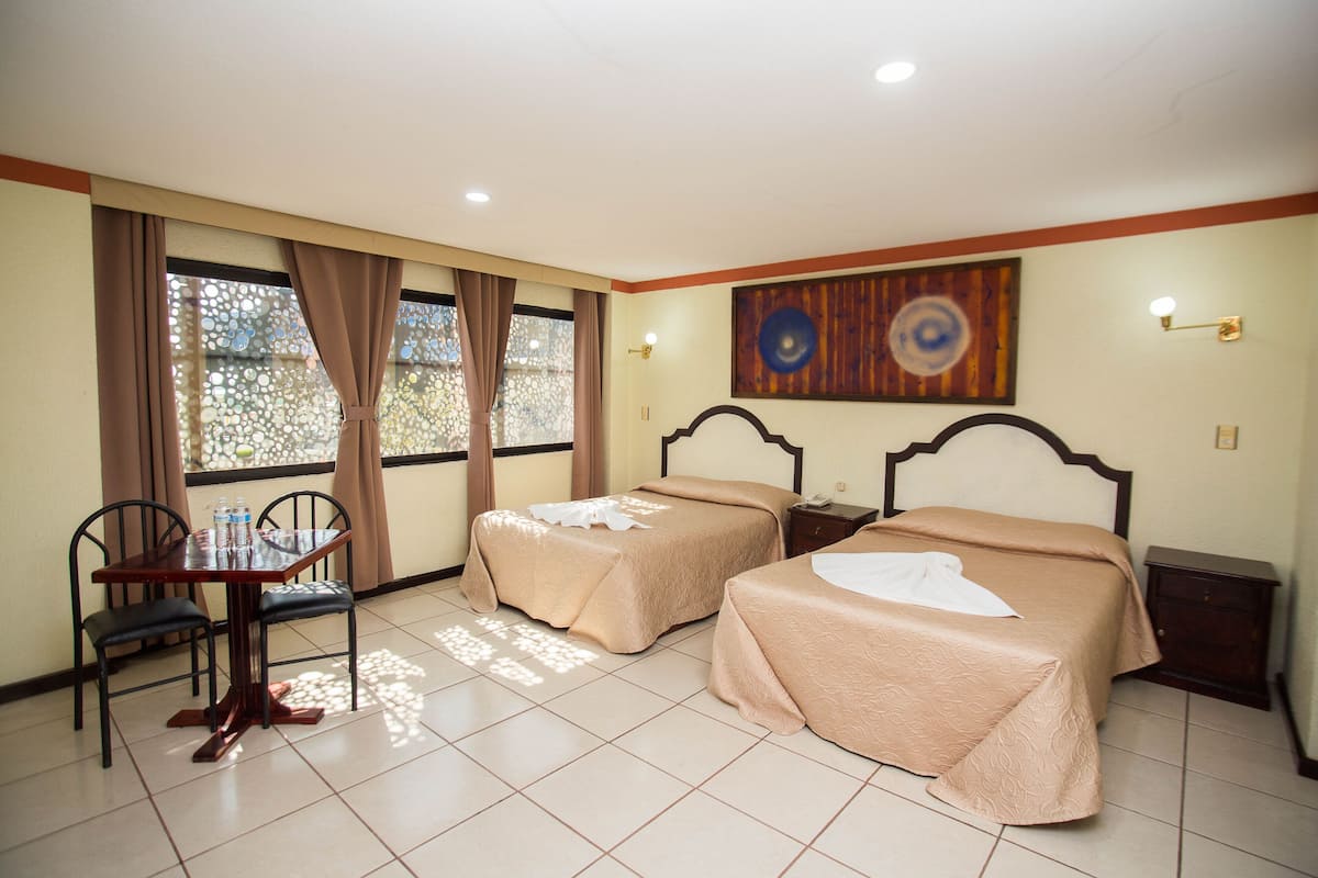 A hotel room with two beds, a dining table with chairs, and a window with curtains.