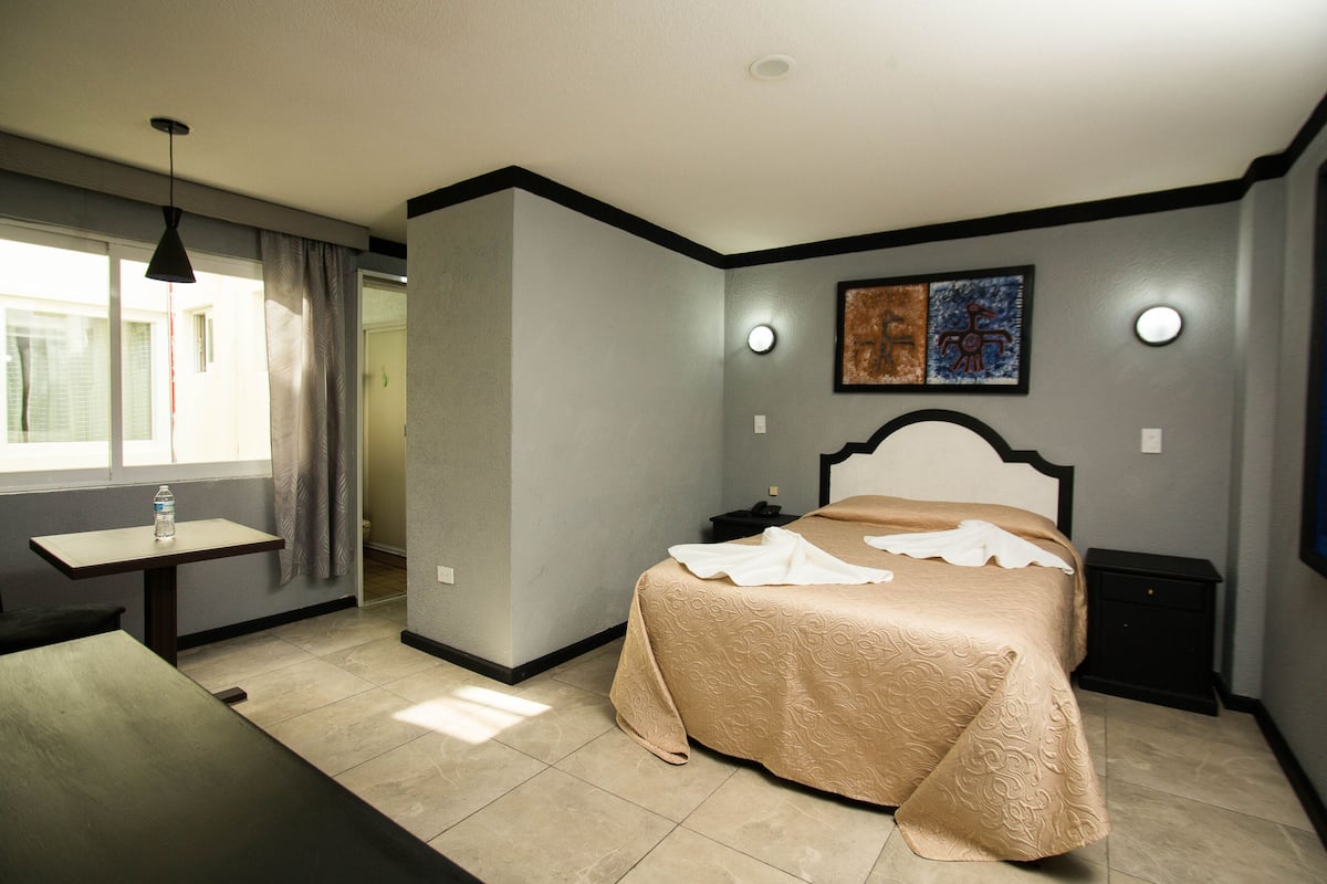 A hotel room with a bed, bedside table, lamp, and artwork on the wall.
