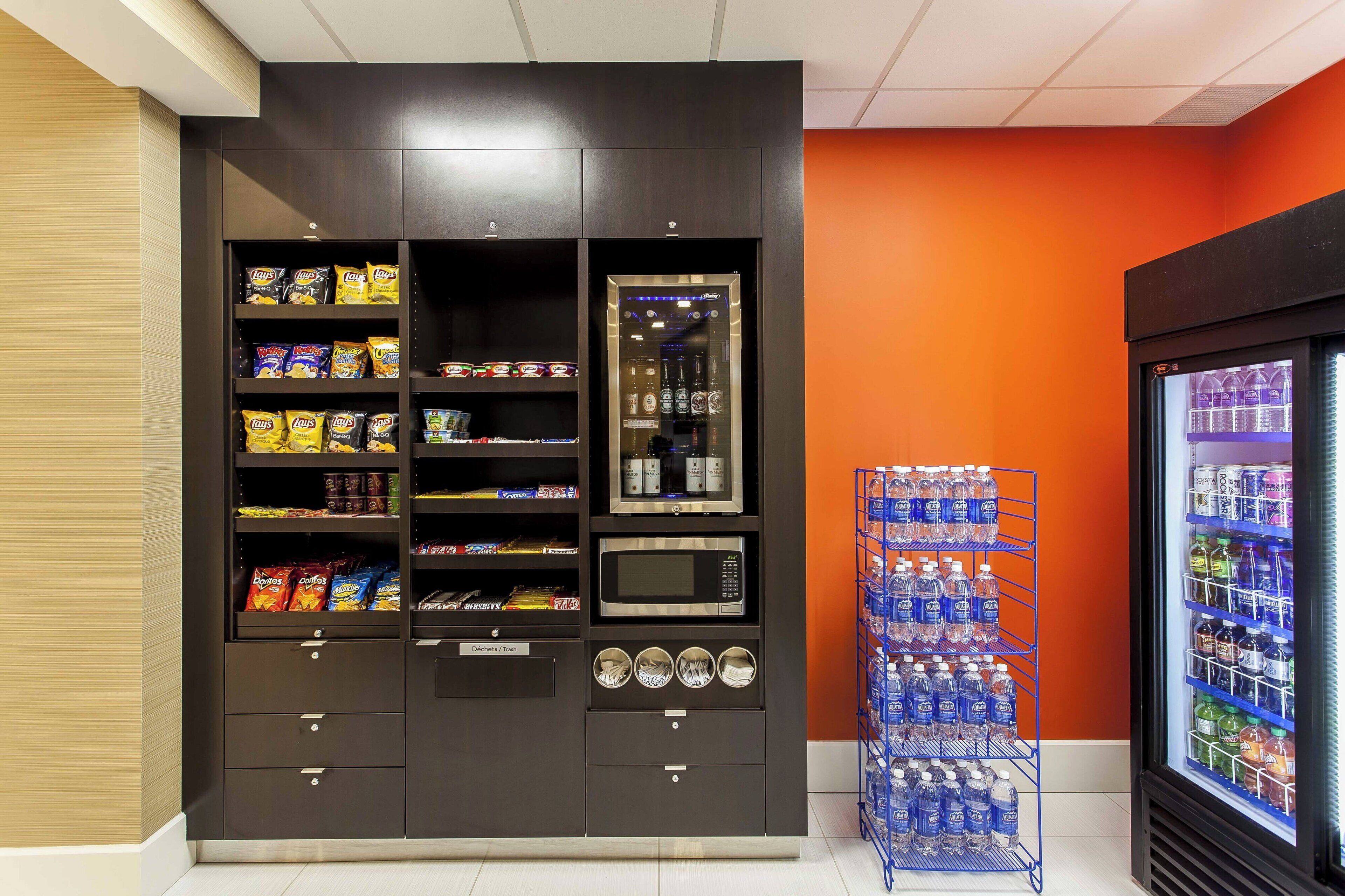 Una máquina expendedora con aperitivos y un microondas, junto a un dispensador de agua y un refrigerador con bebidas.