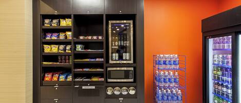 Un distributeur automatique de collations et un four à micro-ondes, situés à côté d’un distributeur d’eau et d’un réfrigérateur rempli de boissons.