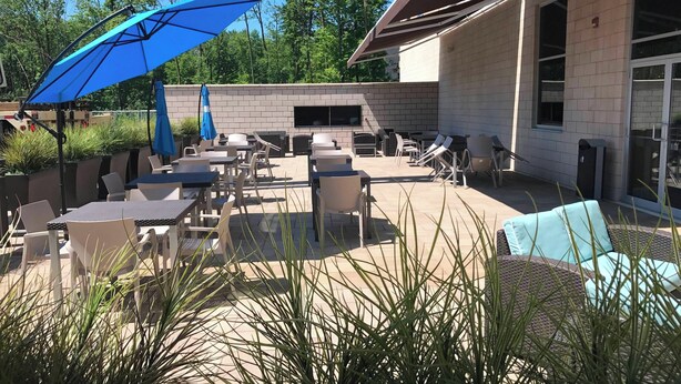 An outdoor patio area with tables and chairs, a blue umbrella, and a fireplace. - Courtyard by Marriott Montreal West Island/Baie D'Urfe (Baie-D'Urfe)