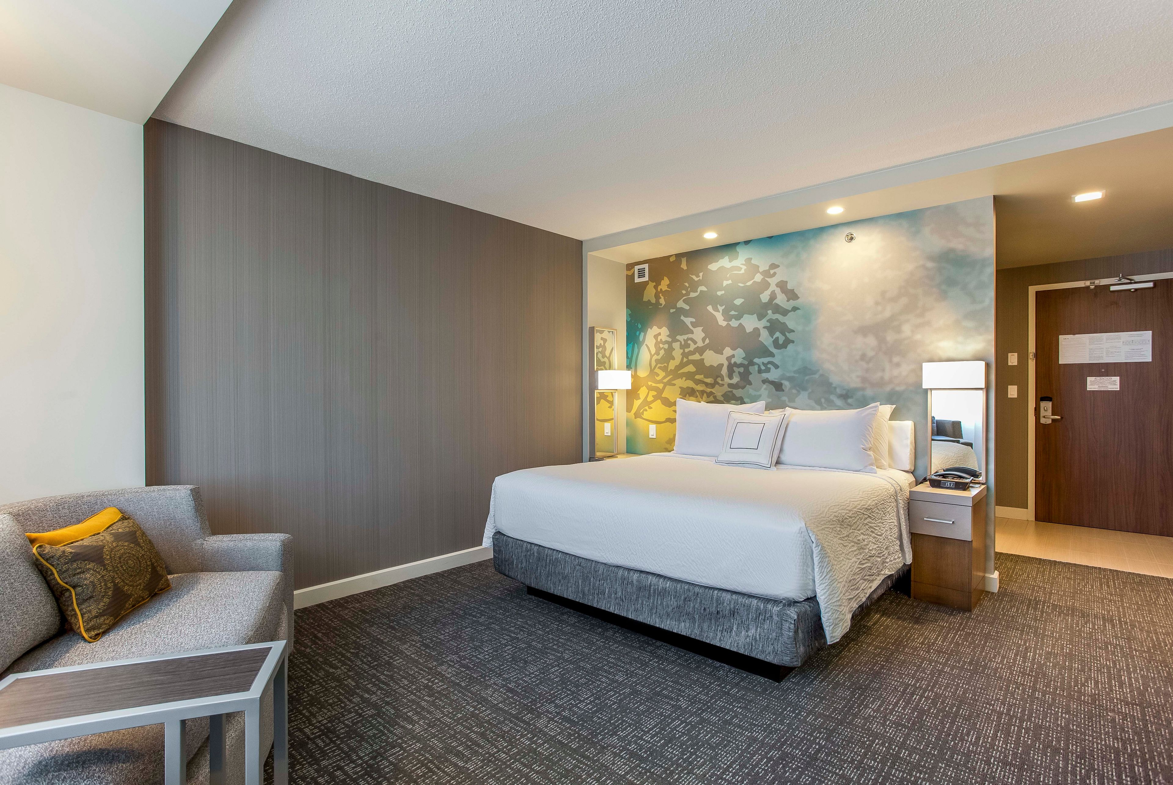 A hotel room with a bed, a desk, a chair, and a nightstand.