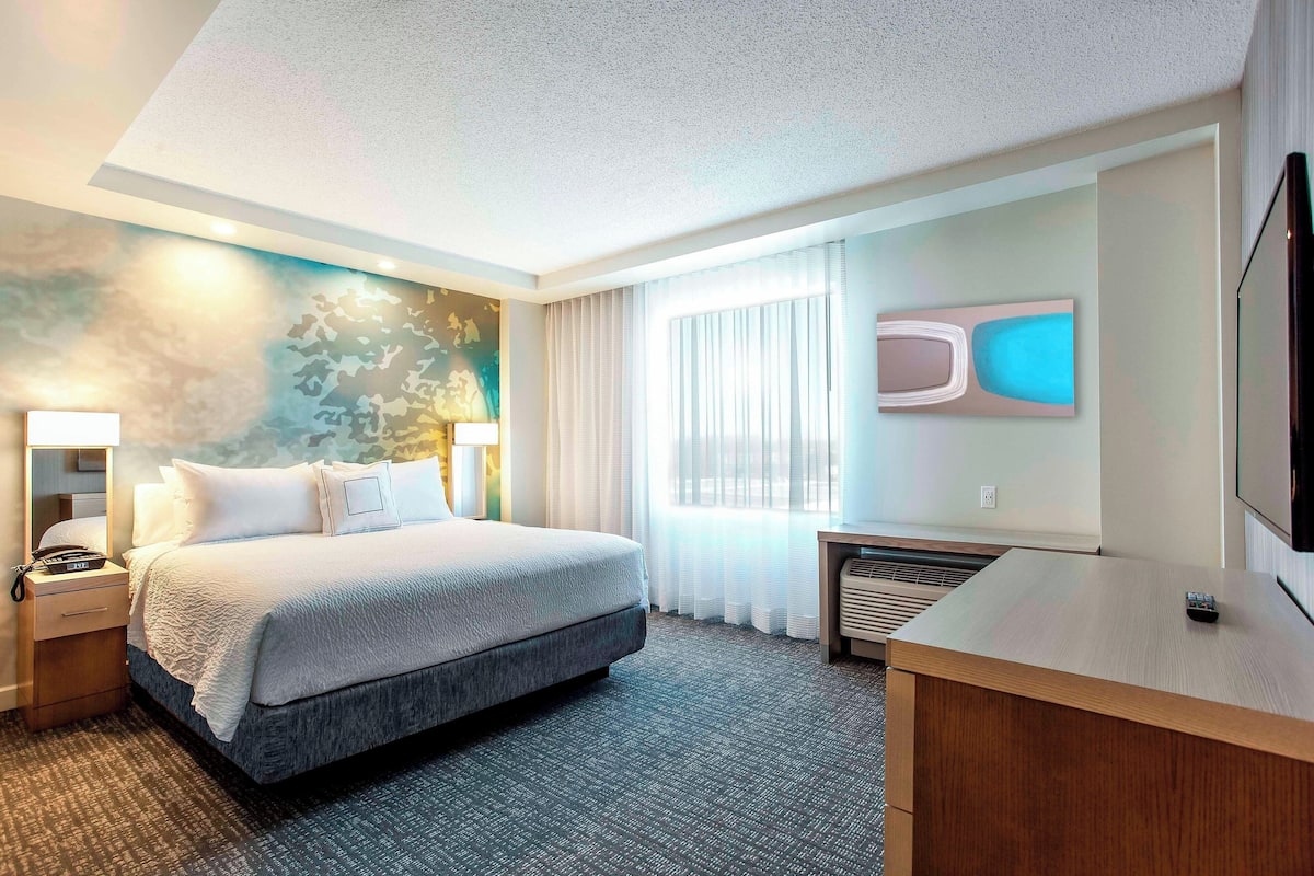 A modern hotel room with a large bed, bedside tables, a desk, and a flat-screen TV.