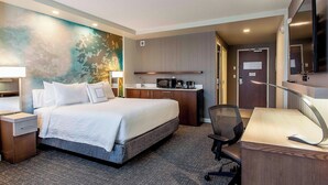 A hotel room with a bed, desk, chair, and kitchenette. - Courtyard by Marriott Montreal West Island/Baie D'Urfe (Baie-D'Urfe)