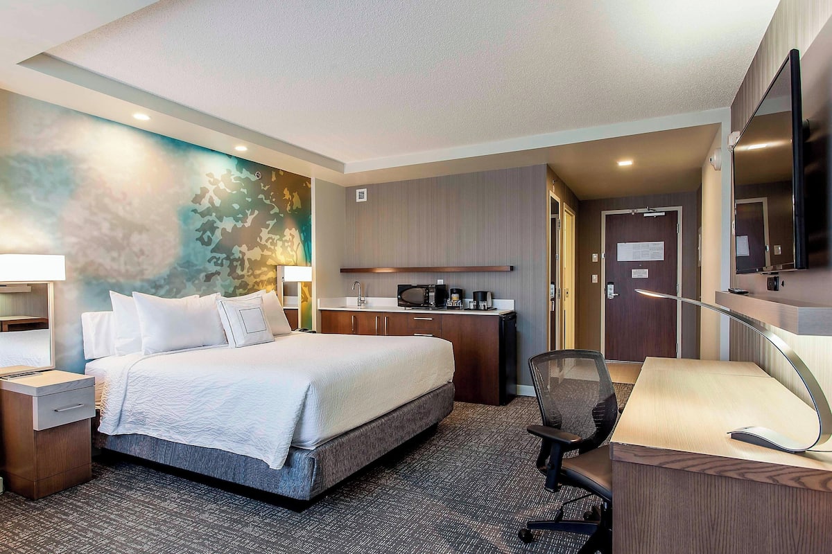 A hotel room with a bed, desk, chair, and kitchenette.
