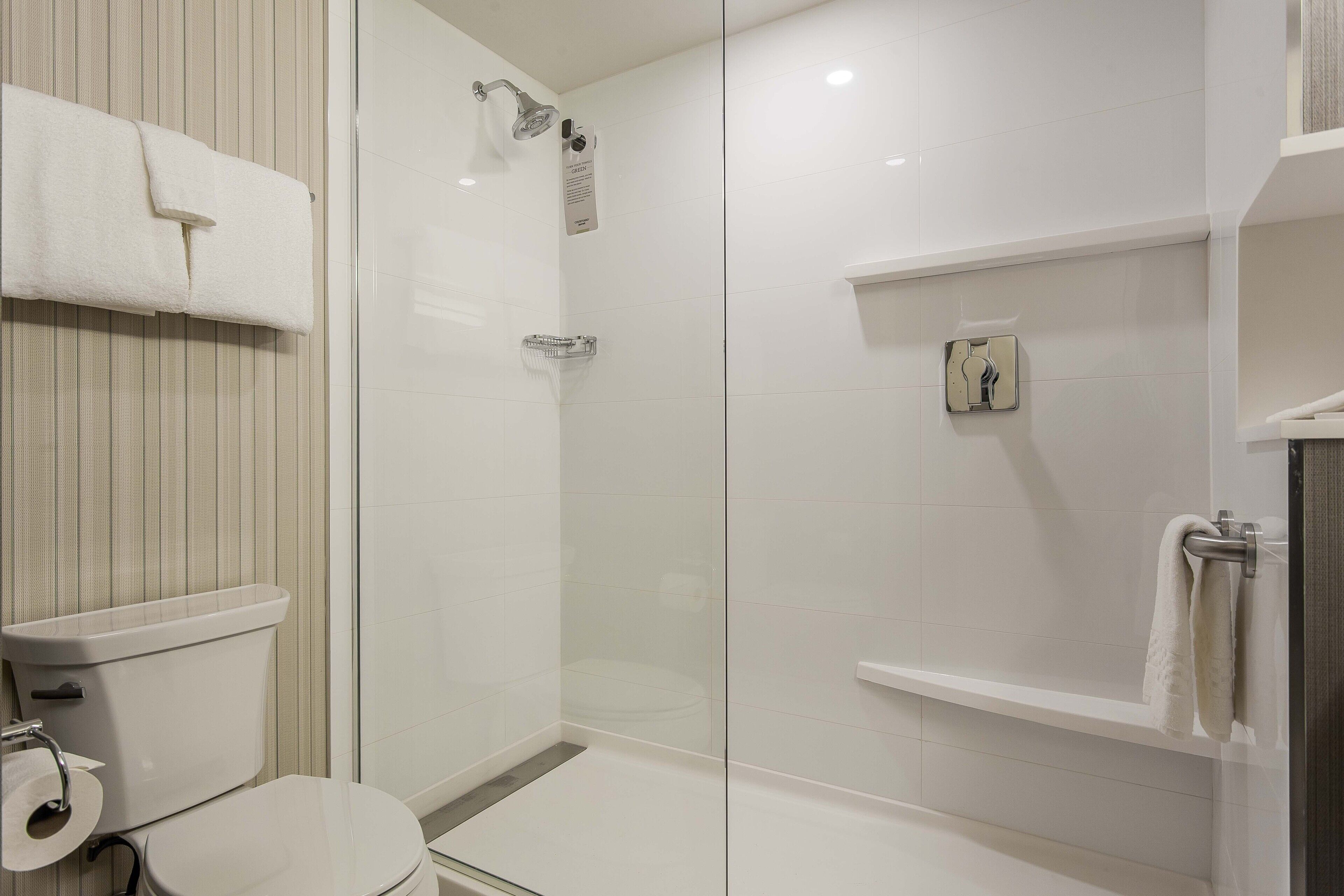 A modern bathroom with a glass-enclosed shower, a toilet, and a shelf with a towel.