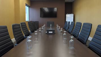 A conference room with a long table, multiple chairs, a projector screen, and a whiteboard.