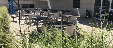 Eine Außenpatio-Terrasse mit Tischen und Stühlen, einem blauen Sonnenschirm und einem Gebäude im Hintergrund.