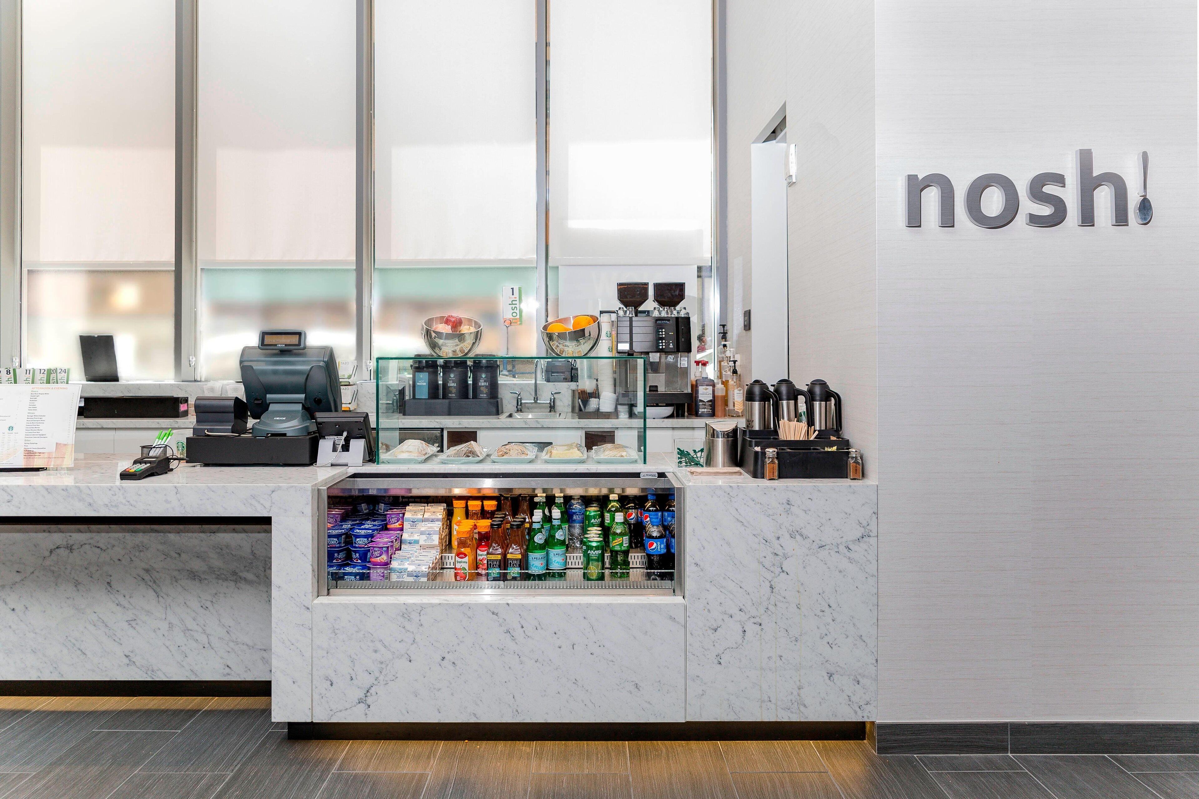 A modern coffee shop counter with a beverage display, a coffee machine, and a menu board.