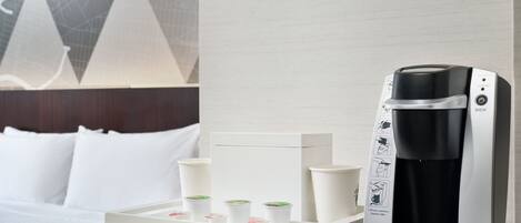 A coffee maker with a tray of disposable cups on a white table in a hotel room.